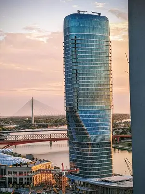 a tall blue building with a bridge in the background at Luxury Belgrade Waterfront top floor Apt with an amazing view in Belgrade