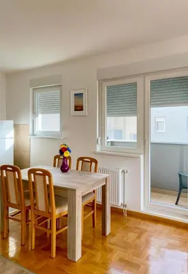 a dining room with a table and chairs and windows at Apartman Kalina in Belgrade