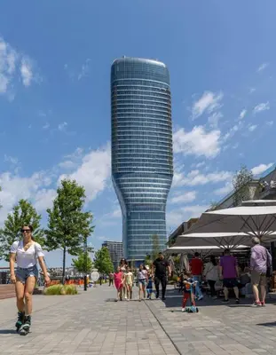 a woman is rollerblading in front of a tall building at 2 Beograd na Vodi Belgrade Waterfront posaljite poruku radi info o nacinu ulaska i preuzimanje kljuca in Belgrade