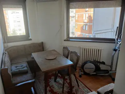 a table and chairs in a room with two windows at Bezanija86 in Belgrade